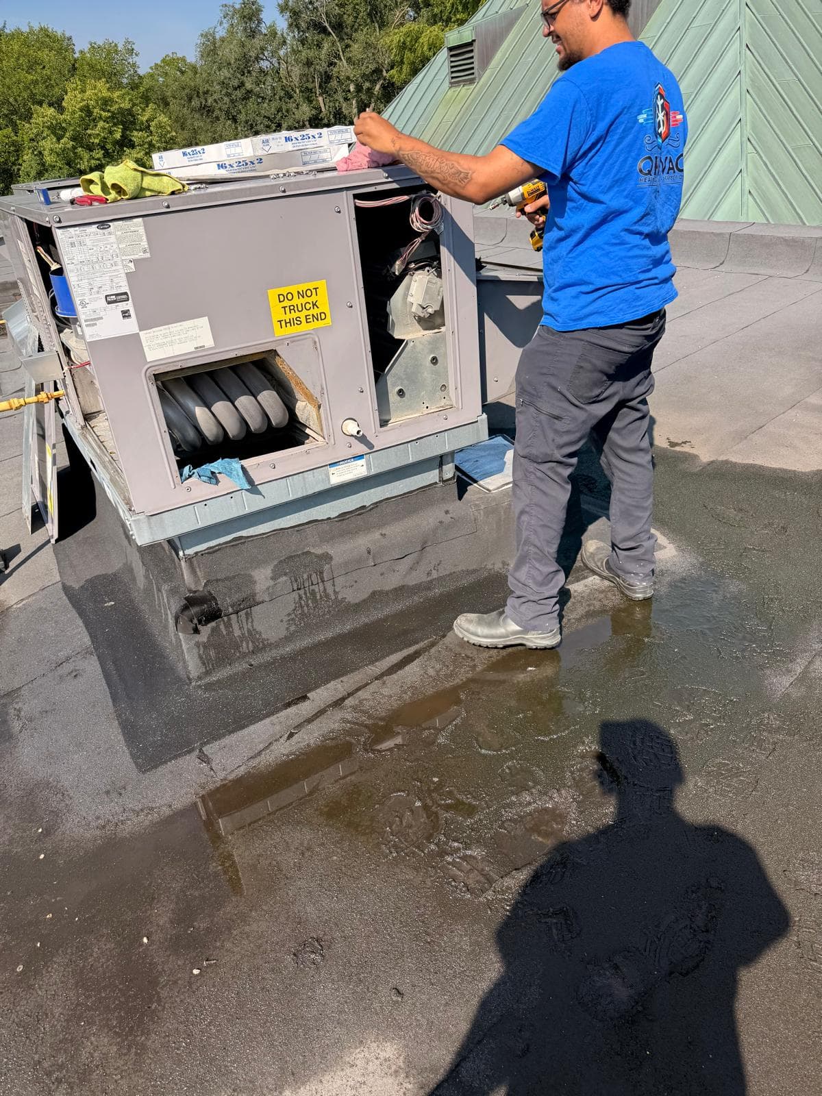 A QP HVAC technician in a branded shirt servicing a rooftop package unit